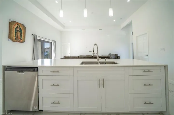 Kitchen with dishwasher, white cabinetry, sink, hanging light fixtures, and french doors