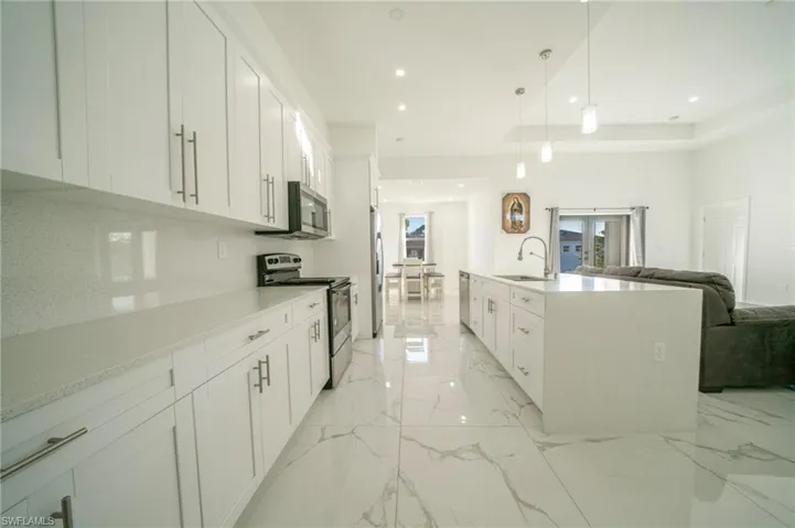 Kitchen featuring sink, appliances with stainless steel finishes, pendant lighting, a kitchen island with sink, and white cabinets