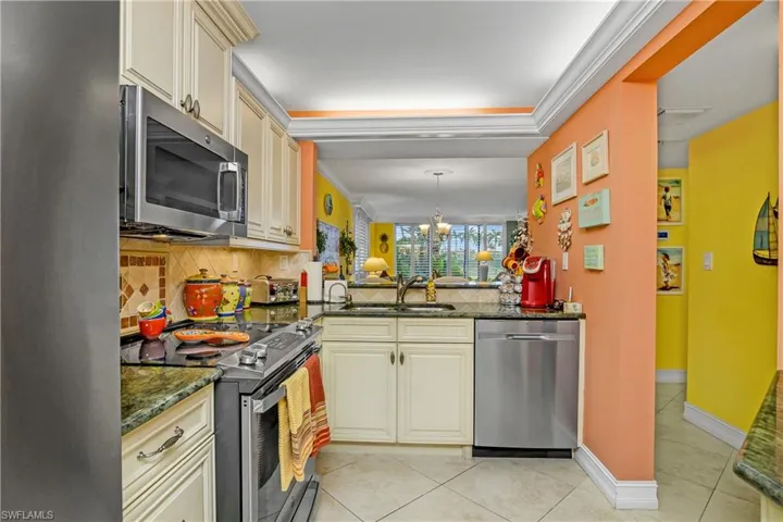 Kitchen featuring appliances with stainless steel finishes, sink, decorative backsplash, cream cabinetry, and light tile patterned flooring