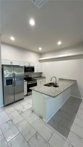 Kitchen featuring white cabinetry, stainless steel appliances, light marble finish floors, dark stone countertops, and recessed lighting