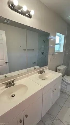 Bathroom featuring double vanity, light marble finish floors, and a marble finish shower