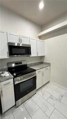 Kitchen featuring stainless steel appliances, white cabinetry, light marble finish flooring, and dark stone counters