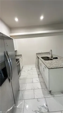 Kitchen featuring light stone countertops, a peninsula, white cabinets, and stainless steel appliances