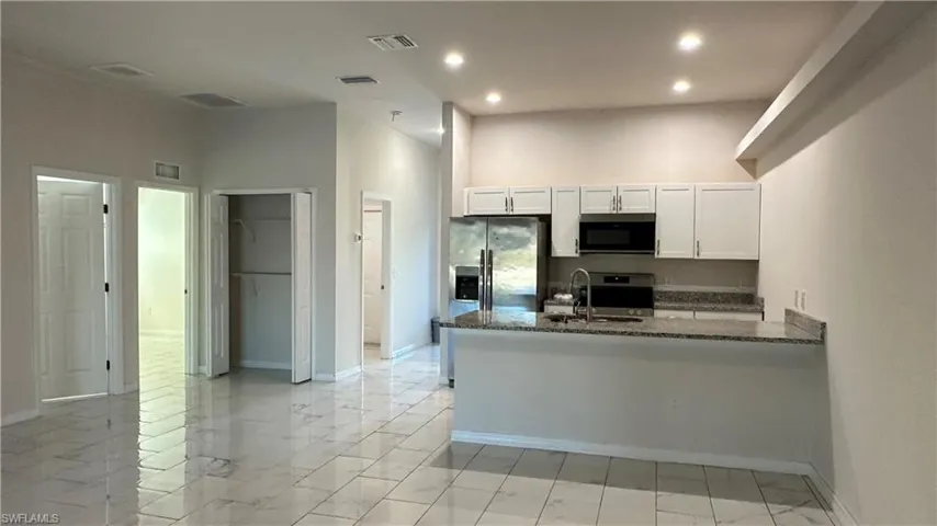 Kitchen with dark stone counters, a peninsula, white cabinets, stainless steel appliances, and light marble finish floors