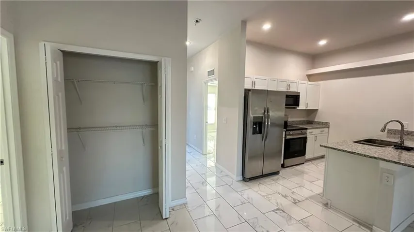 Kitchen featuring stainless steel appliances, white cabinets, light stone countertops, light marble finish flooring, and recessed lighting