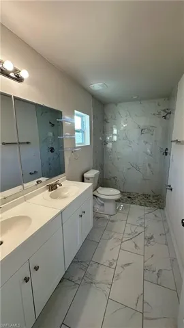 Bathroom featuring double vanity, a marble finish shower, and light marble finish flooring