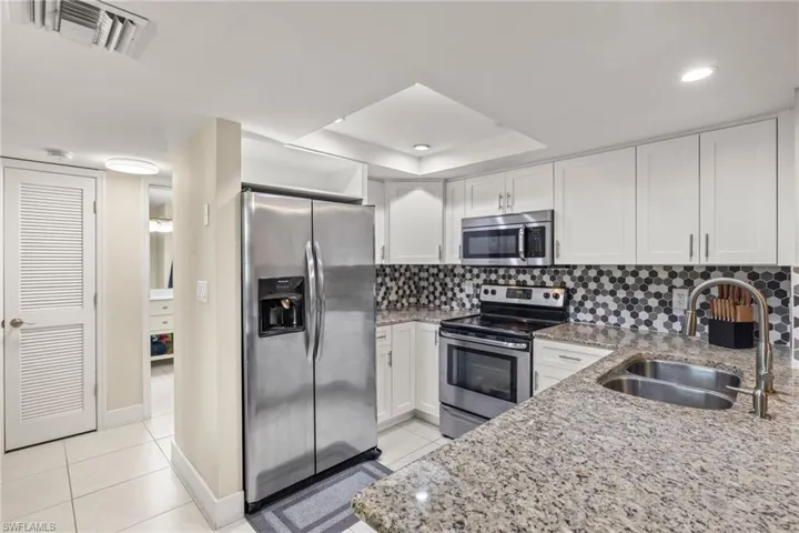 Kitchen featuring white cabinetry, decorative backsplash, sink, light stone counters, and appliances with stainless steel finishes