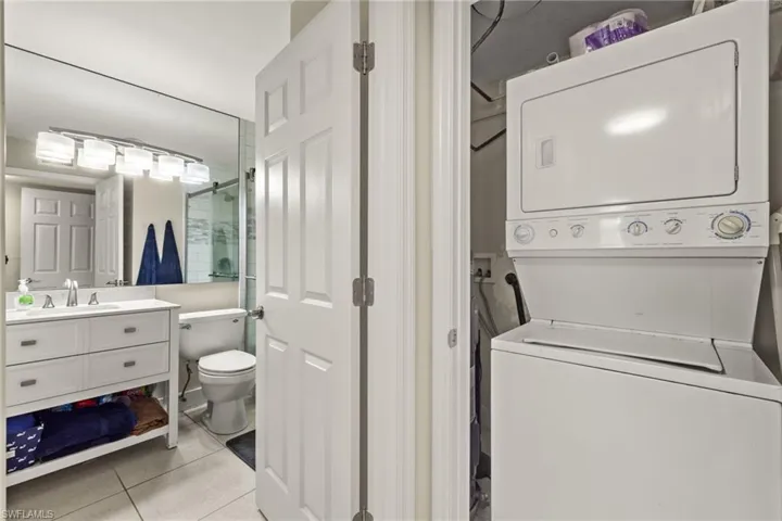 Laundry area featuring stacked washer and clothes dryer, light tile patterned flooring, and sink