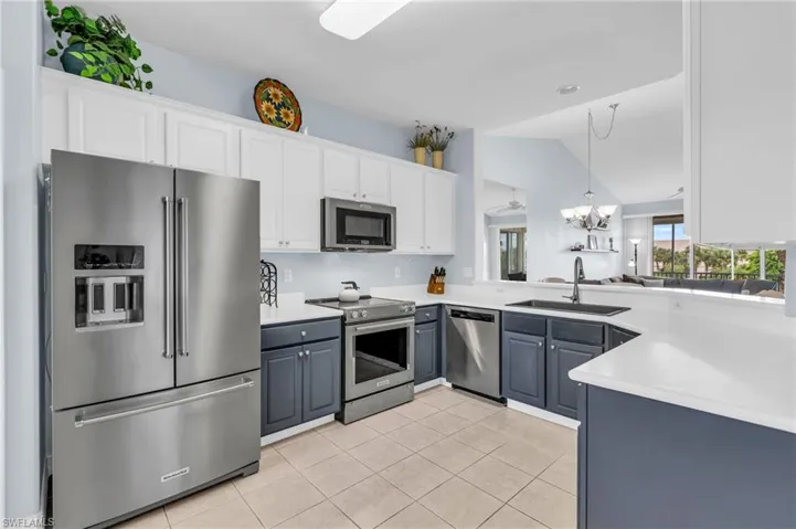Kitchen with pendant lighting, sink, lofted ceiling, appliances with stainless steel finishes, and white cabinetry