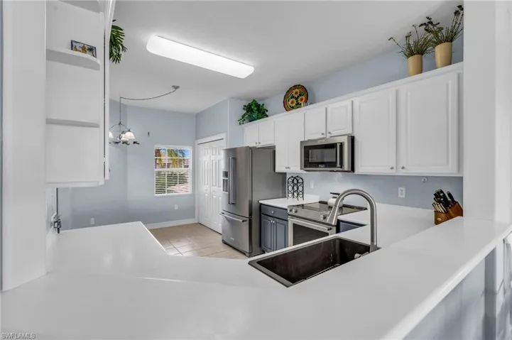 Kitchen with stainless steel appliances, white cabinets, light tile patterned flooring, hanging light fixtures, and a chandelier