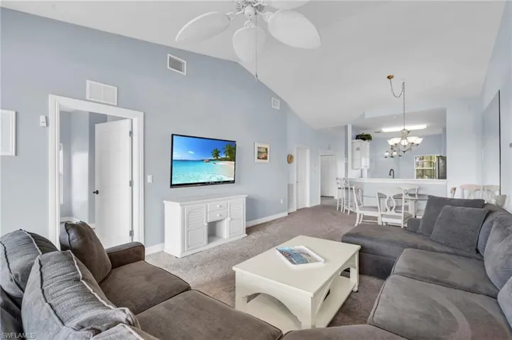 Living room featuring ceiling fan with notable chandelier, lofted ceiling, and carpet