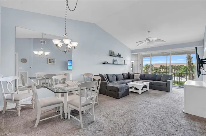 Carpeted dining space with ceiling fan with notable chandelier and high vaulted ceiling