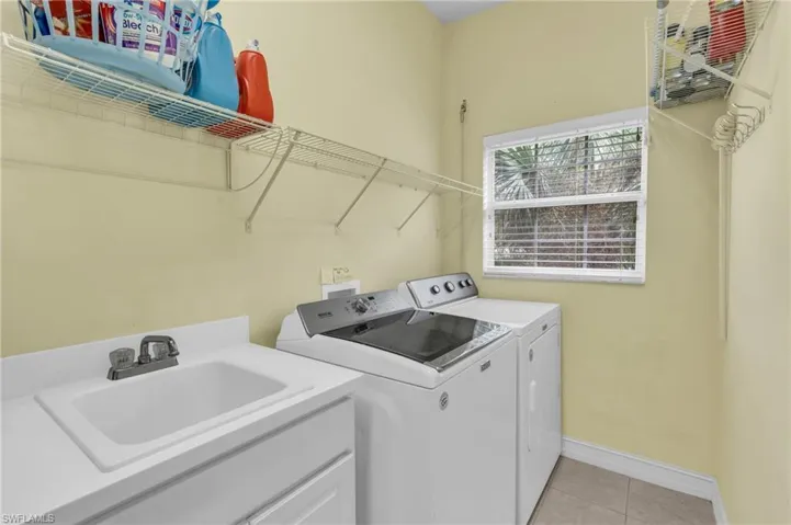 Washroom with sink, independent washer and dryer, and light tile patterned flooring