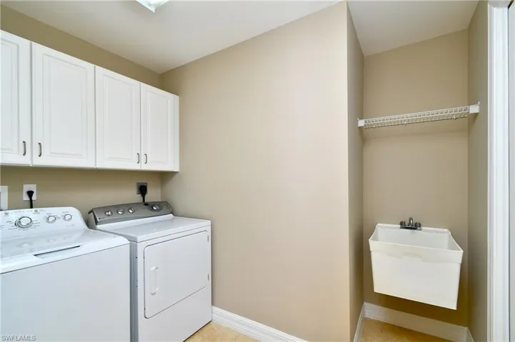 Laundry room featuring washer and dryer, light tile flooring, laundry sink and cabinets