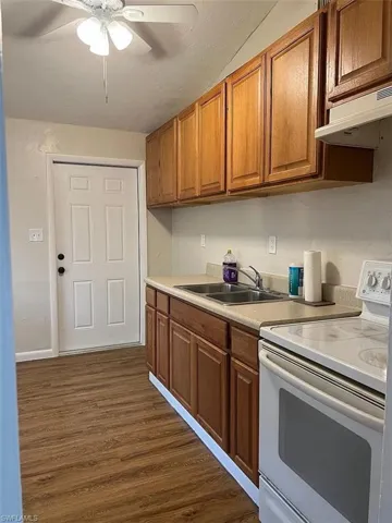 Kitchen featuring brown cabinets, dark wood-type flooring, white electric range, under cabinet range hood, and a sink