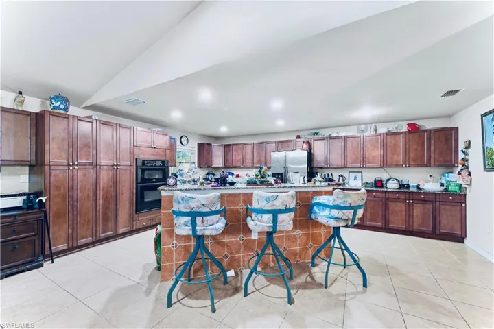 Kitchen with stainless steel fridge, light tile patterned floors, a center island, recessed lighting, and a kitchen bar