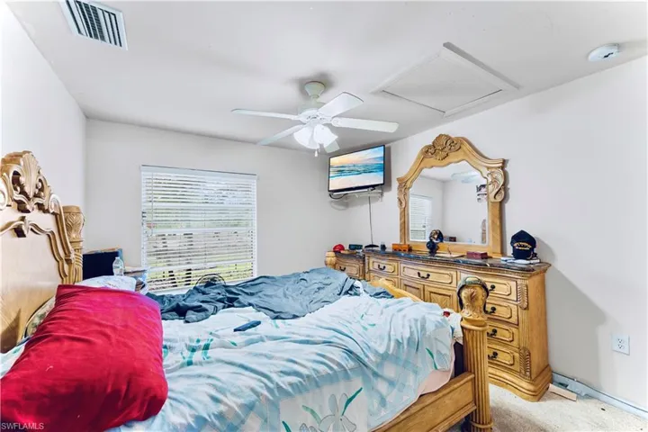 Bedroom featuring attic access, multiple windows, light colored carpet, and a ceiling fan