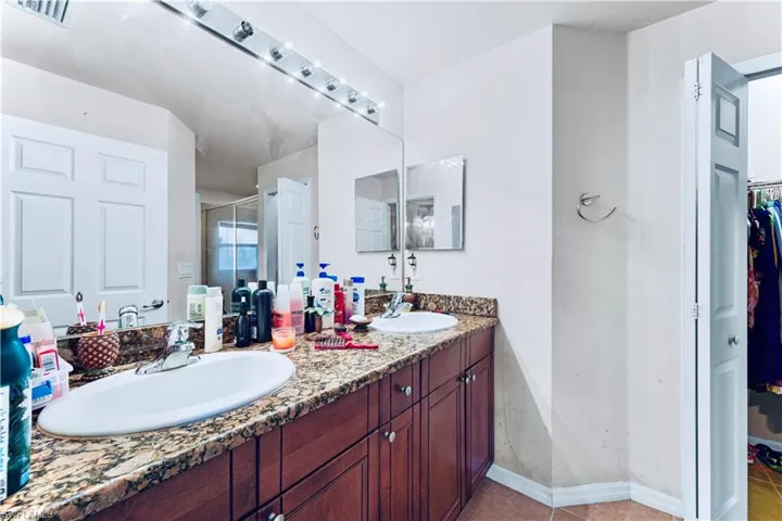 Bathroom with double vanity, a walk in closet, a shower stall, and tile patterned flooring