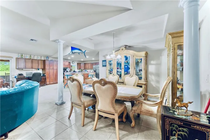 Dining area with ornate columns, a raised ceiling, and light tile patterned flooring