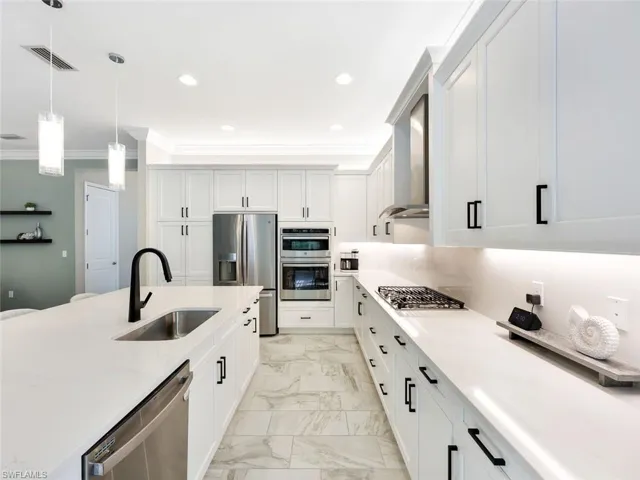 Kitchen with white cabinets, sink, light stone countertops, appliances with stainless steel finishes, and decorative light fixtures