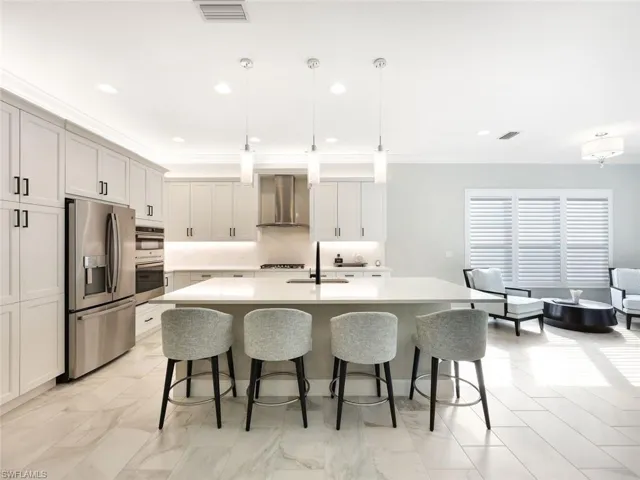 Kitchen featuring a kitchen island with sink, wall chimney range hood, hanging light fixtures, sink, and appliances with stainless steel finishes