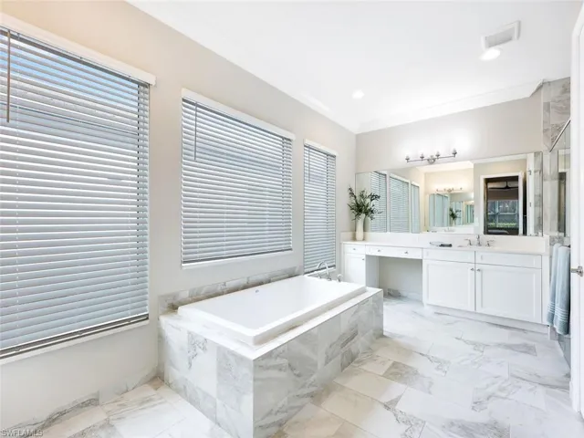 Bathroom with vanity, a relaxing tiled tub, plenty of natural light, and ornamental molding