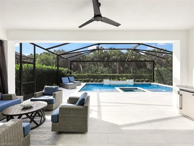 View of pool featuring glass enclosure, an in ground hot tub, a patio, and an outdoor hangout area