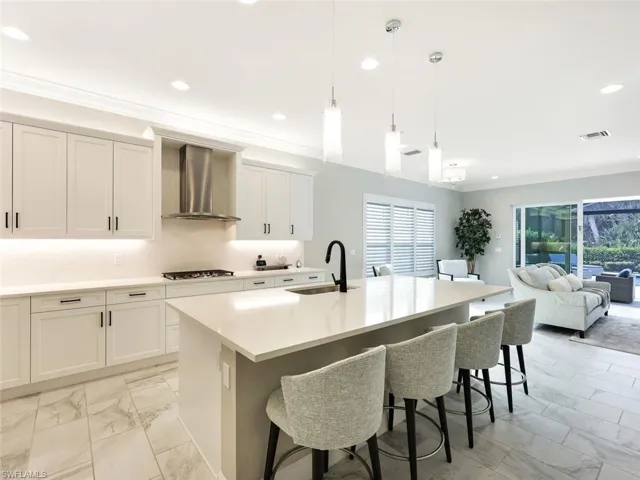 Kitchen featuring gas cooktop, wall chimney exhaust hood, a kitchen island with sink, sink, and hanging light fixtures
