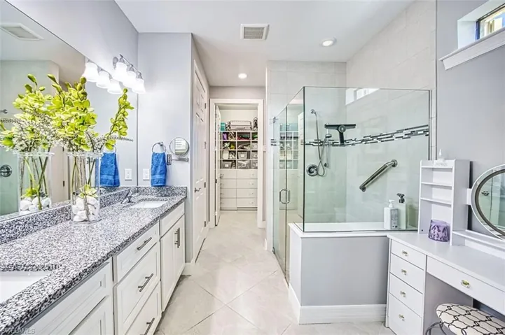 Bathroom featuring a shower stall, double vanity, a walk in closet, recessed lighting, and light tile patterned flooring