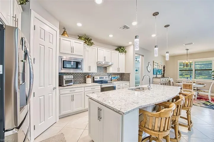 Kitchen with pendant lighting, stainless steel appliances, a kitchen island with sink, white cabinets, and a kitchen bar