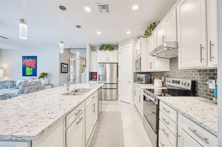 Kitchen featuring stainless steel appliances, white cabinetry, hanging light fixtures, light stone countertops, and recessed lighting