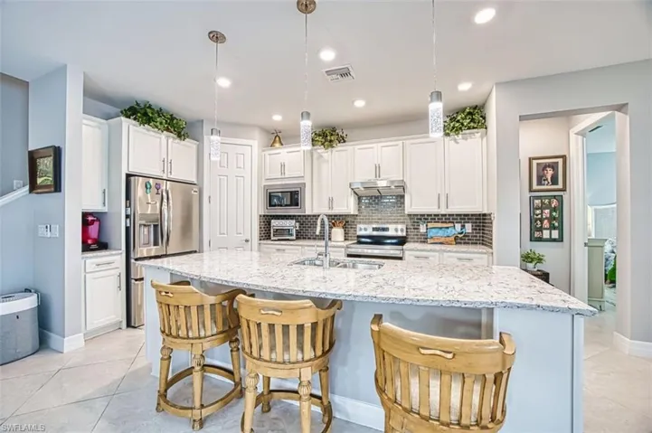 Kitchen featuring hanging light fixtures, stainless steel appliances, white cabinets, a kitchen breakfast bar, and recessed lighting