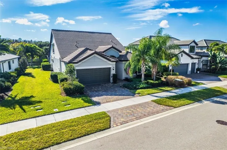 View of front of home with a front yard, a tile roof, decorative driveway, a garage, and stucco siding