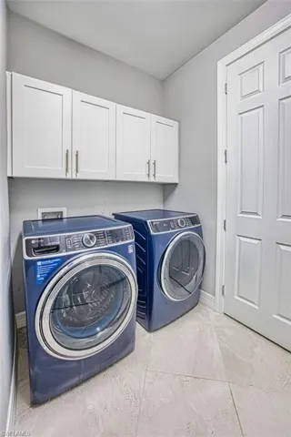 Laundry area with cabinet space, independent washer and dryer, and light tile patterned floors
