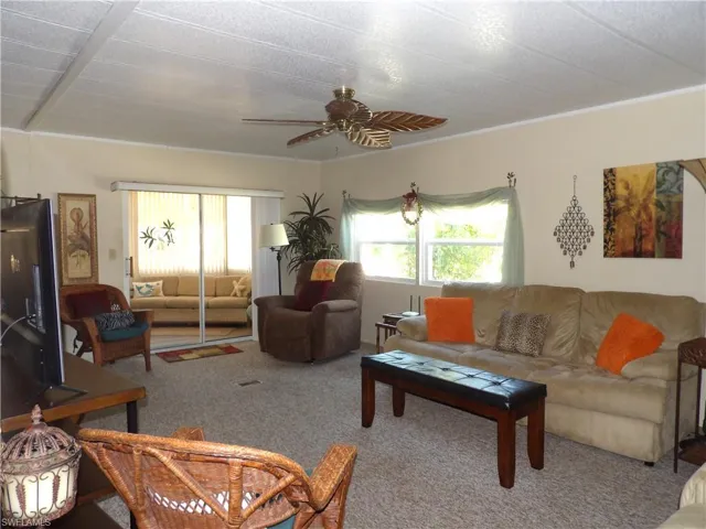 Living area featuring carpet flooring, plenty of natural light, a ceiling fan, and ornamental molding