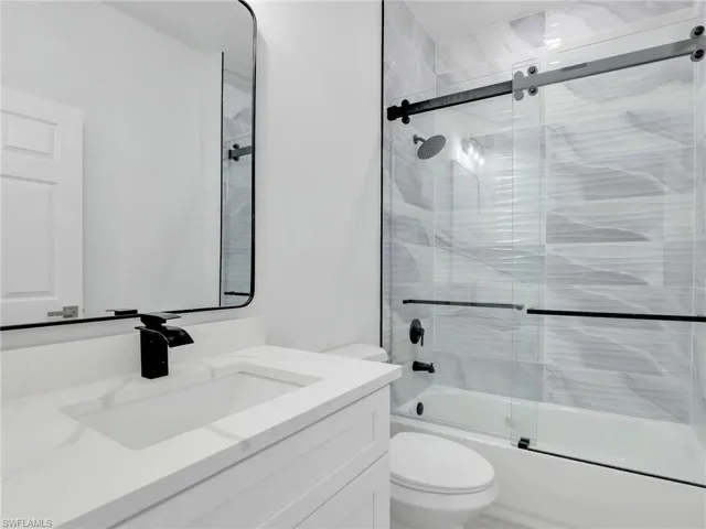 Full bathroom featuring bath / shower combo with glass door, toilet, and vanity