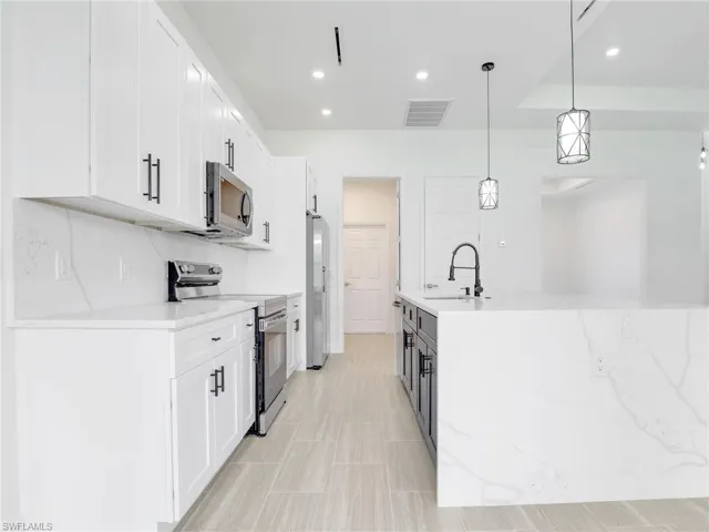 Kitchen with sink, hanging light fixtures, white cabinetry, and stainless steel appliances