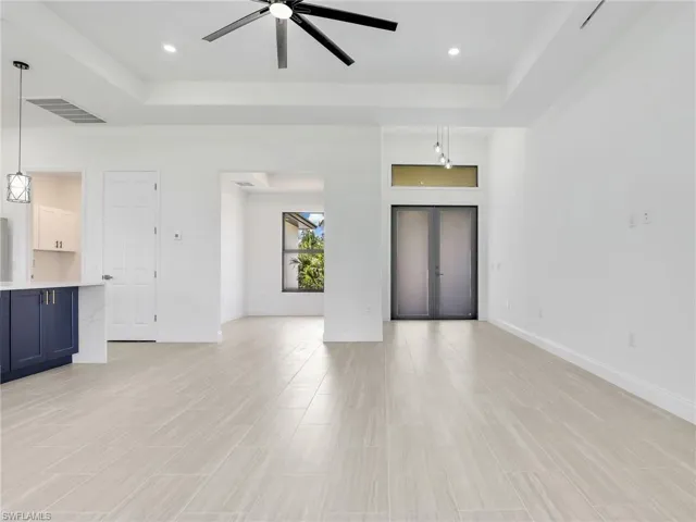 Unfurnished living room with light tile flooring, ceiling fan, and a raised ceiling