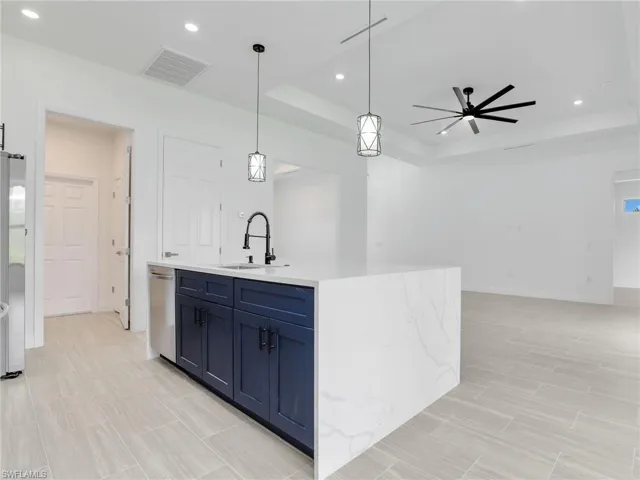 Kitchen featuring ceiling fan, a tray ceiling, hanging light fixtures, sink, and a kitchen island with sink