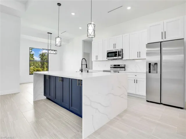 Kitchen featuring appliances with stainless steel finishes, white cabinets, backsplash, and hanging light fixtures