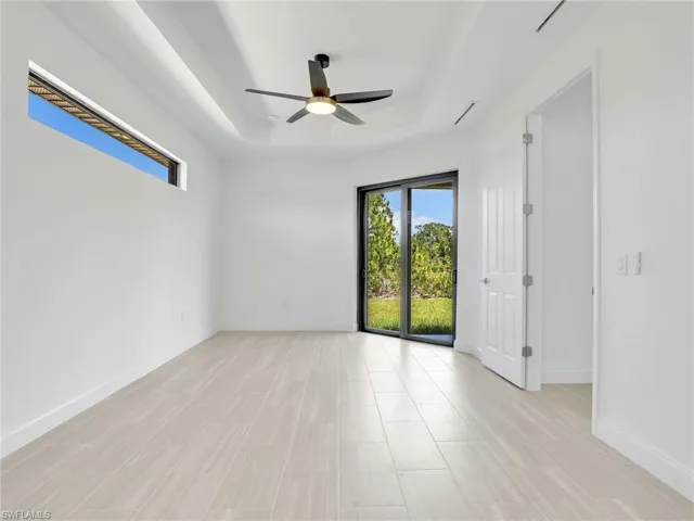 Empty room featuring ceiling fan, a raised ceiling, and light tile flooring