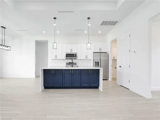 Kitchen with stainless steel appliances, white cabinets, blue cabinets, and pendant lighting