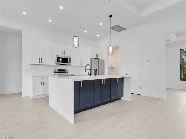 Kitchen featuring hanging light fixtures, appliances with stainless steel finishes, white cabinets, a kitchen island with sink, and light tile floors