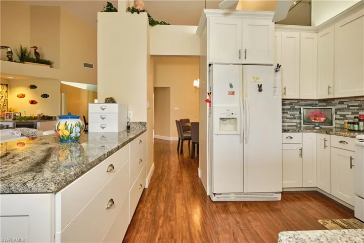 Kitchen with white refrigerator with ice dispenser, dark wood finished floors, and light stone countertops