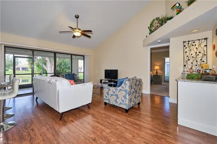 Living area featuring high vaulted ceiling, ceiling fan, baseboards, and wood finished floors