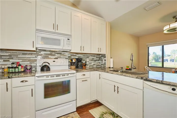Kitchen featuring visible vents, backsplash, a sink, dark stone counters, and white appliances