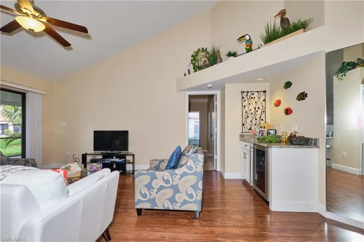 Living area with a bar, a healthy amount of sunlight, wine cooler, and dark wood-type flooring