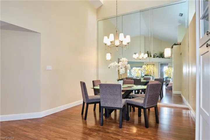 Dining area featuring a chandelier, high vaulted ceiling, wood finished floors, and baseboards