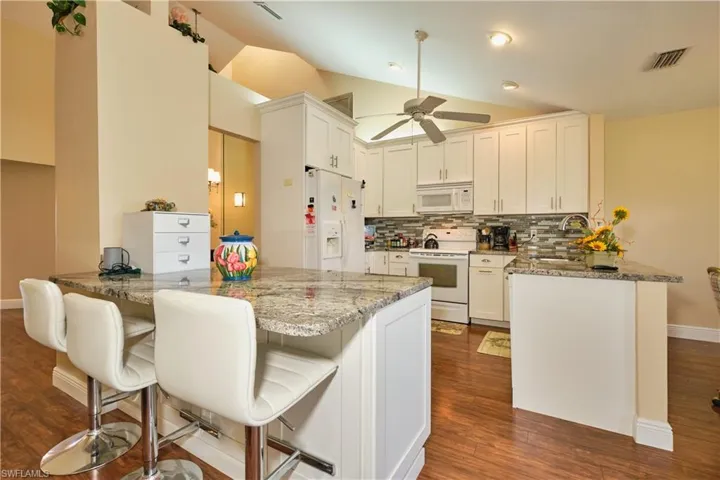 Kitchen featuring lofted ceiling, visible vents, a sink, white appliances, and a peninsula