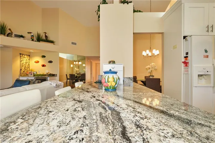 Kitchen with high vaulted ceiling, a notable chandelier, white refrigerator with ice dispenser, visible vents, and light stone countertops